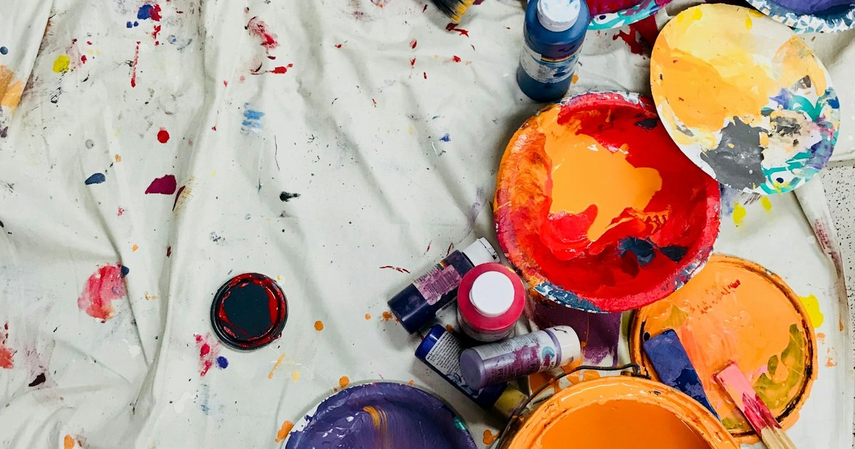 Pinturas y pinceles de colores variados dispuestos sobre una lona blanca, materiales de trabajo creativo en un espacio de taller