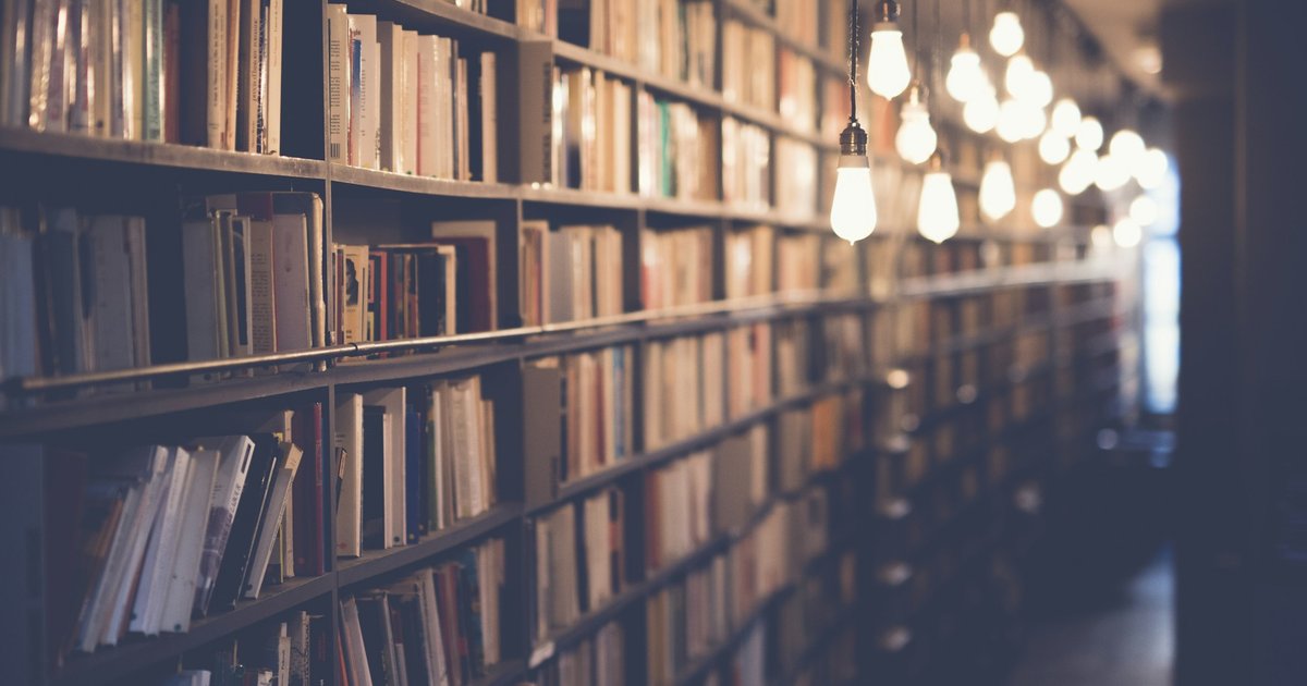 Interior de una biblioteca con iluminación cálida e incandescente, estanterías de libros y ambiente íntimo de conocimiento acumulado