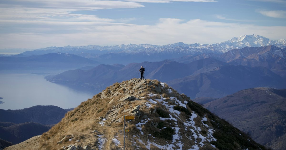 Senderista en la cima de una montaña contemplando un panorama de picos y lagos en los Dolomitas italianos