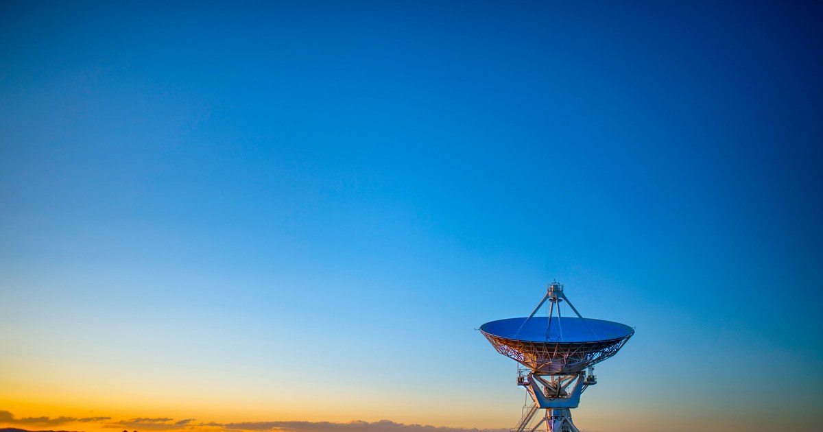 Radiotelescopio del Very Large Array en Nuevo México al amanecer, apuntando al cielo con luz dorada en el horizonte