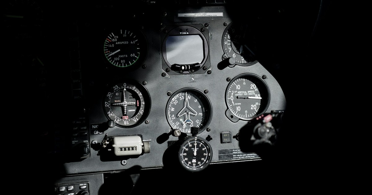Panel de instrumentos de cabina de vuelo con múltiples indicadores analógicos: velocímetro, indicador de rumbo, velocidad vertical. Iluminación dramática sobre fondo oscuro.