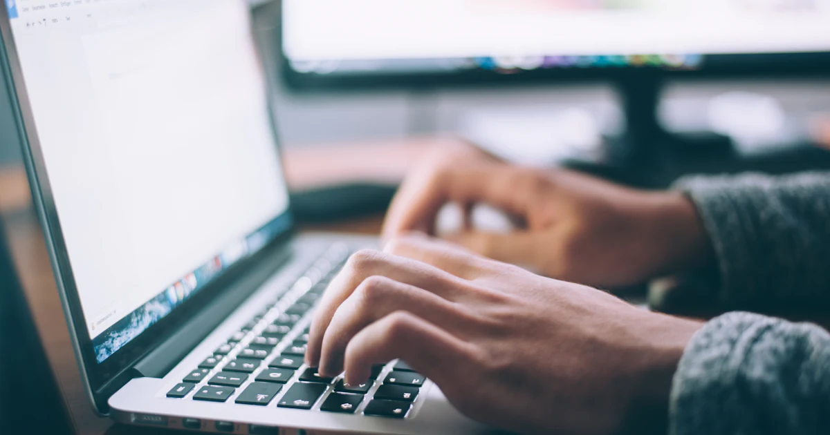 Hands typing on a laptop keyboard in a minimalist work setting